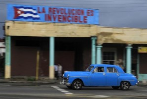 A 1949 Dodge car used as a taxi drives under a banner reading "The revolution is invincible" in Havana