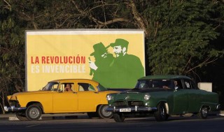 Vintage cars drive near a banner with image of Cuban late rebel revolutionary Camilo Cienfuegos and Cuba's former president Fidel Castro in Havana
